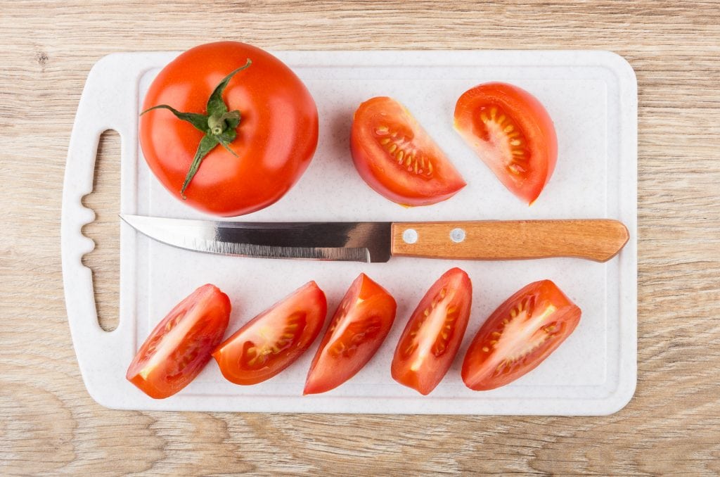 Pieces of red tomatoes and kitchen knife on cutting board