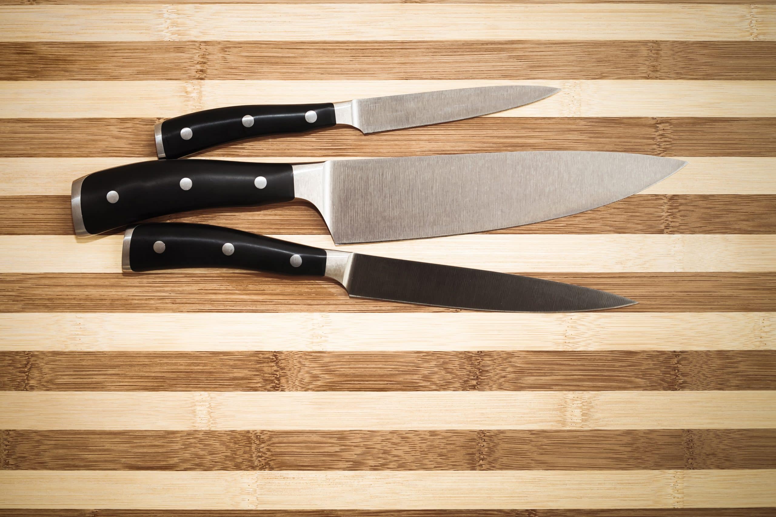 Three utility kitchen knifes on a wooden- cutting board
