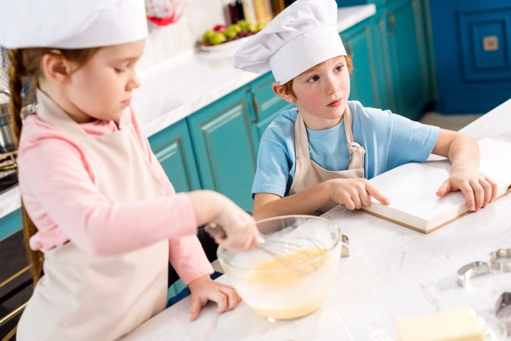 2 children in the kitchen with chef hats on their heads