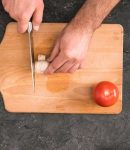 A cutting board on which a mushroom is cut. There is a marble background with olive oil, salt, pepper, eggs, olives and milk