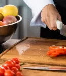 chef-cutting-bell-pepper-near-knifes-and-vegetables-in-kitchen-e1647855731670