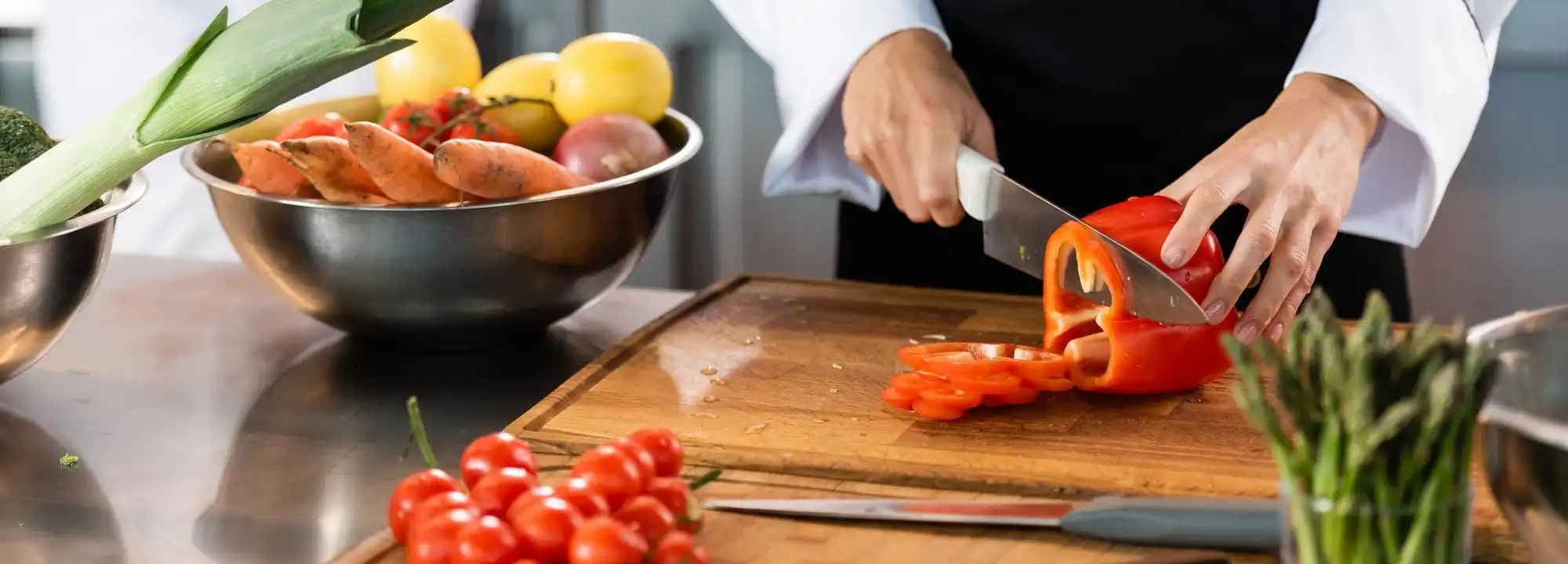 chef-cutting-bell-pepper-near-knifes-and-vegetables-in-kitchen-e1647855731670