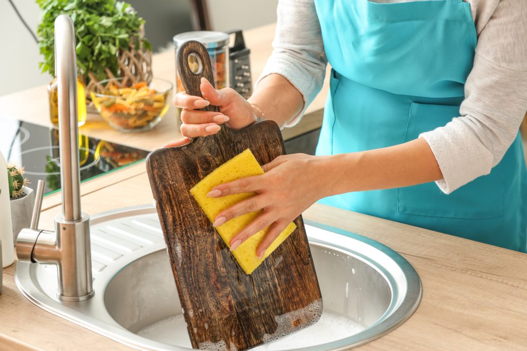 Woman washing wooden board in kitchen sink — P