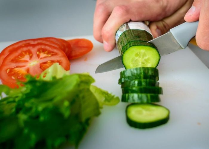 Left handed man cutting cucumber, tomato and sal