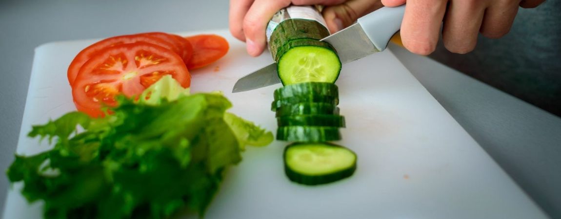 Left handed man cutting cucumber, tomato and sal