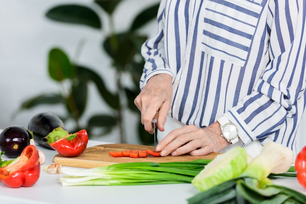 Cropped image of senior woman cutting red bell p