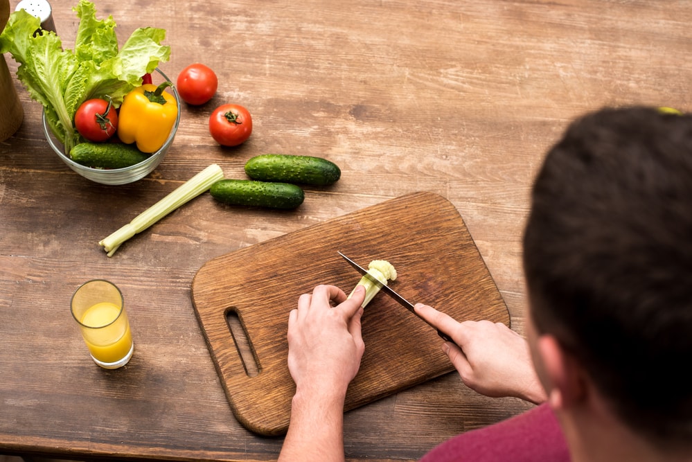 Selective focus of man cutting celery on wooden chop