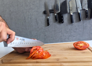 The Mac Professional 8 Inch Hollow Edge Chef Knife, held by our tester, while execeuting a soft tomato test on a cutting board