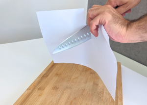 The Mac Professional 8 Inch Hollow Edge Chef Knife, held by our tester, while execeuting a paper test on a cutting board