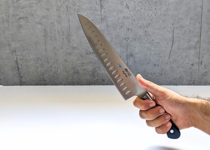 The Mac Professional 8 Inch Hollow Edge Chef Knife, held by our tester, on a white canvas and gray wall