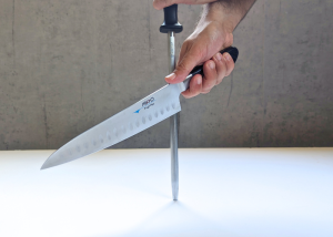 The Mac Professional 8 Inch Hollow Edge Chef Knife, held by our tester, while sharpened with a honing rod on a white canvas and gray wall