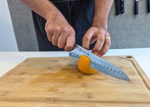 The Mac Professional 8 Inch Hollow Edge Chef Knife, held by our tester, while peeling a orange on a cutting board