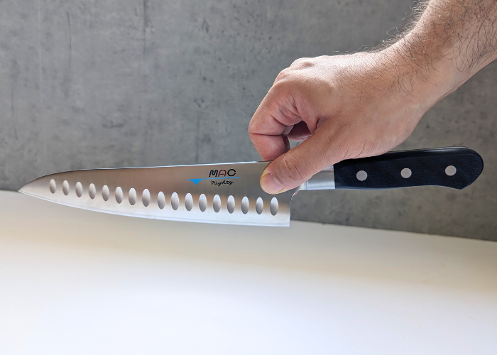 The Mac Professional 8 Inch Hollow Edge Chef Knife, held by our tester, usinh a pinch grip on a white canvas and gray wall