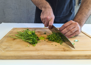 The Mac Professional 8 Inch Hollow Edge Chef Knife, held by our tester, while chopping herbs on a cutting board
