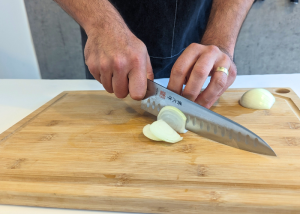 The Mac Professional 8 Inch Hollow Edge Chef Knife, held by our tester, while chopping onion on a cutting board