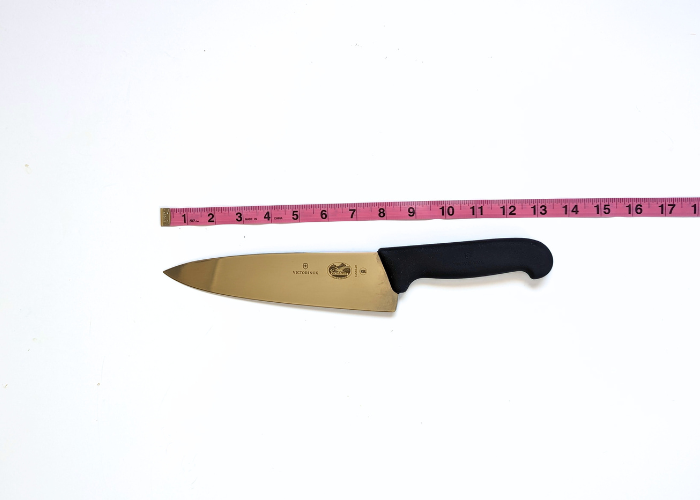 The Victorinox Fibrox Pro, horizontal on a white background while measured with a pink ruler at