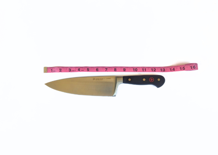 The wusthof classic 8 inch extra wide, horizontal on a white background while measured with a pink ruler at 12.4 inches