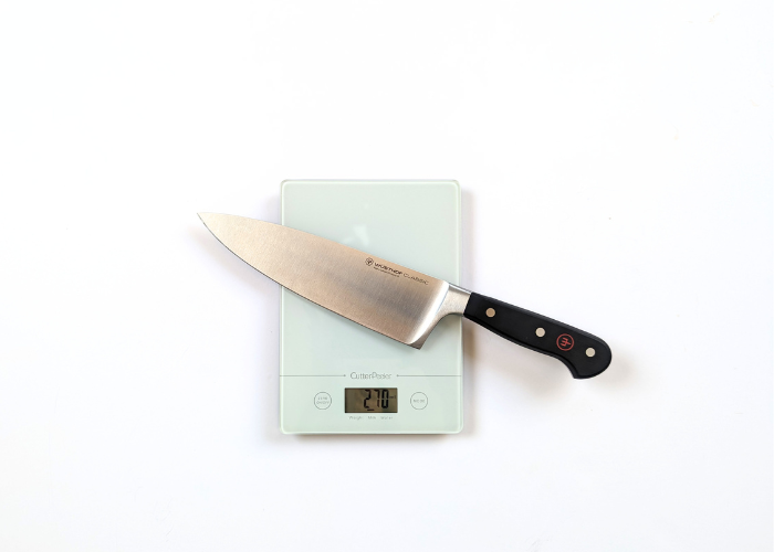 The wusthof classic 8 inch extra wide, diagonal on a white background while weighted on a white digital scales at 9.7 ounces