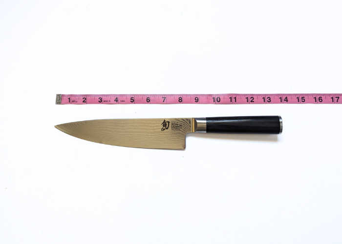 The shun knife, horizontal on a white background while measured with a pink ruler at