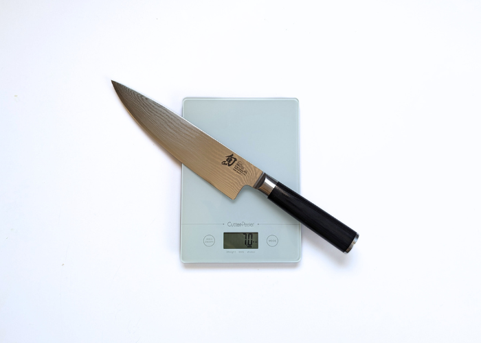 The shun knife, diagonal on a white background while weighted on a white digital scales at