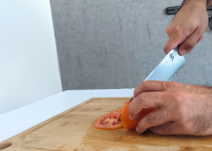 The shun knife, held by our tester, while execeuting a soft tomato test on a cutting board