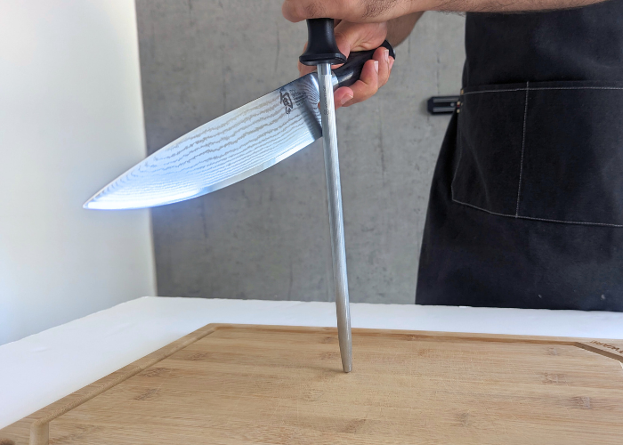 The shun knife, held by our tester, while sharpened with a honing rod on a white canvas and gray wall