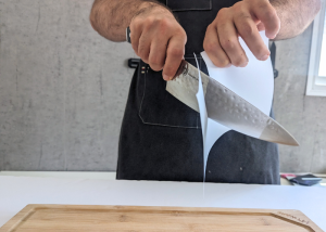 The Dalstrong, held by our tester, while execeuting a paper test on a cutting board