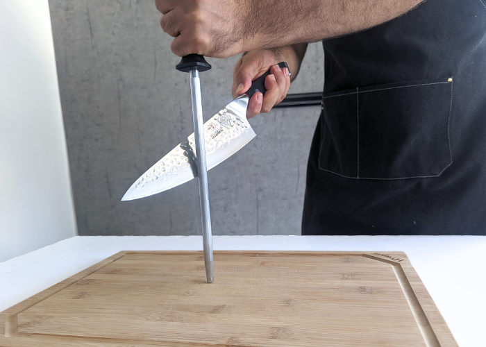 The Dalstrong, held by our tester, while sharpened with a honing rod on a white canvas and gray wall