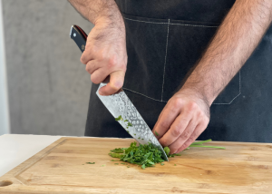 The Dalstrong, held by our tester, while chopping herbs on a cutting board