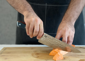 The Dalstrong, held by our tester, while cutting a sweet potato on a cutting board