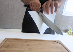 The Tojiro Fujitora DP, held by our tester, while execeuting a paper test on a cutting board