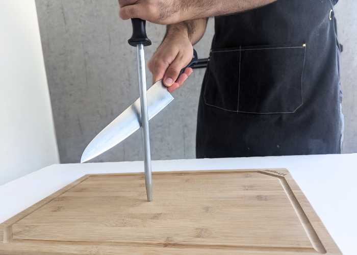 The Tojiro Fujitora DP, held by our tester, while sharpened with a honing rod on a white canvas and gray wall